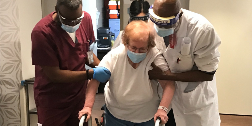 Short term rehab patient with chronic pain walking with walker being assisted by two staff persons