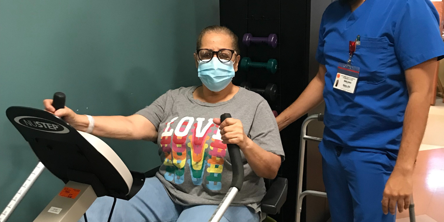 Short term rehab patient riding an incumbent bike with a physical therapist standing beside her.