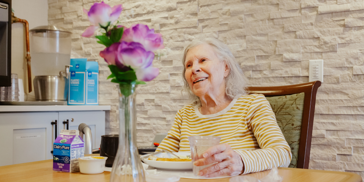 Photo of smiling senior woman enjoying a healthy meal at the dining room table in a skilled nursing facility